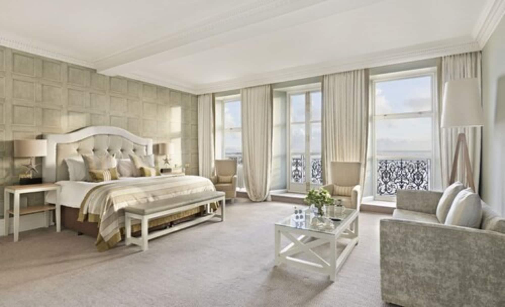 The Grand Brighton Hotell Exteriör bild The photo shows a spacious and elegantly decorated hotel room or suite. It features a large bed with a tufted headboard, adorned with plush pillows and a decorative bedspread. The room has light-colored walls, possibly with a textured pattern, and la