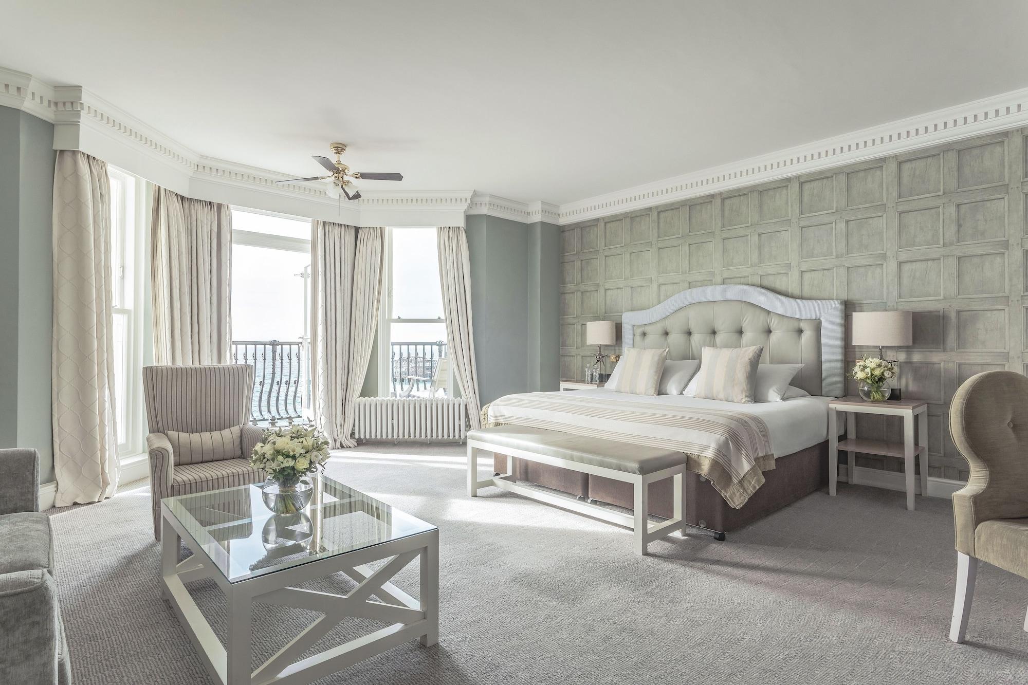 The Grand Brighton Hotell Exteriör bild The photo shows a spacious and elegantly designed hotel room. It features a large bed with light-colored bedding and a decorative headboard. On either side of the bed, there are small nightstands with lamps. There are two comfortable armchairs positi