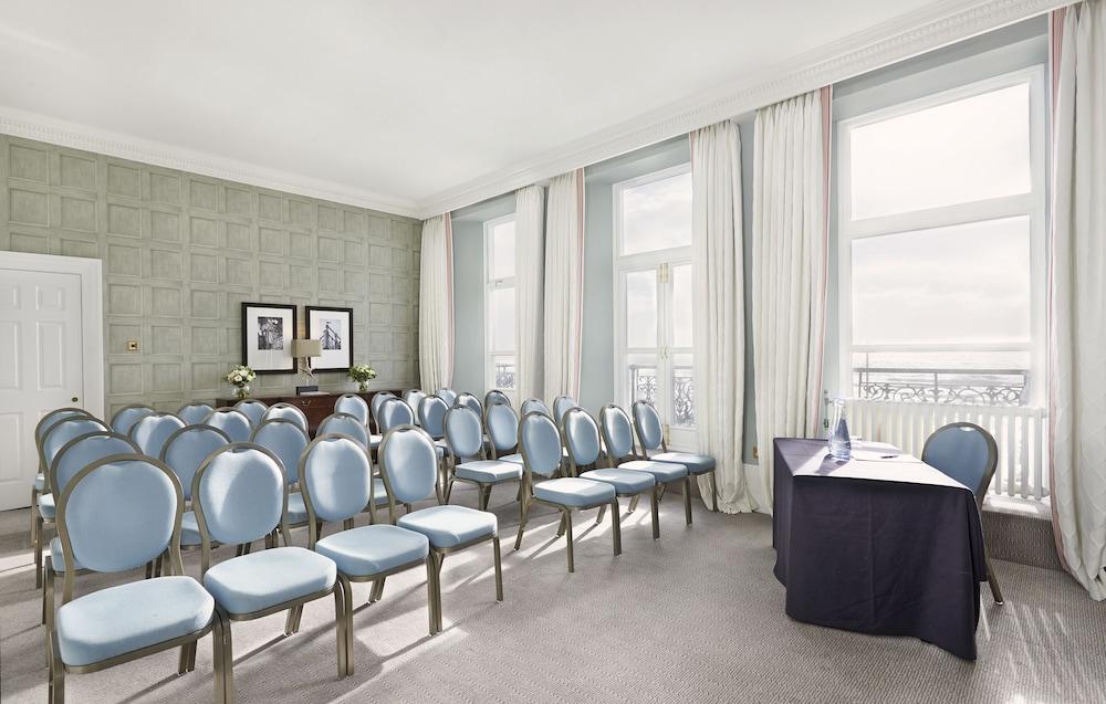 The Grand Brighton Hotell Exteriör bild The photo shows a well-lit meeting room with a modern and elegant design. There are several rows of blue chairs arranged neatly in front of a table covered with a dark cloth, likely intended for a speaker or presenter. The room features large windows