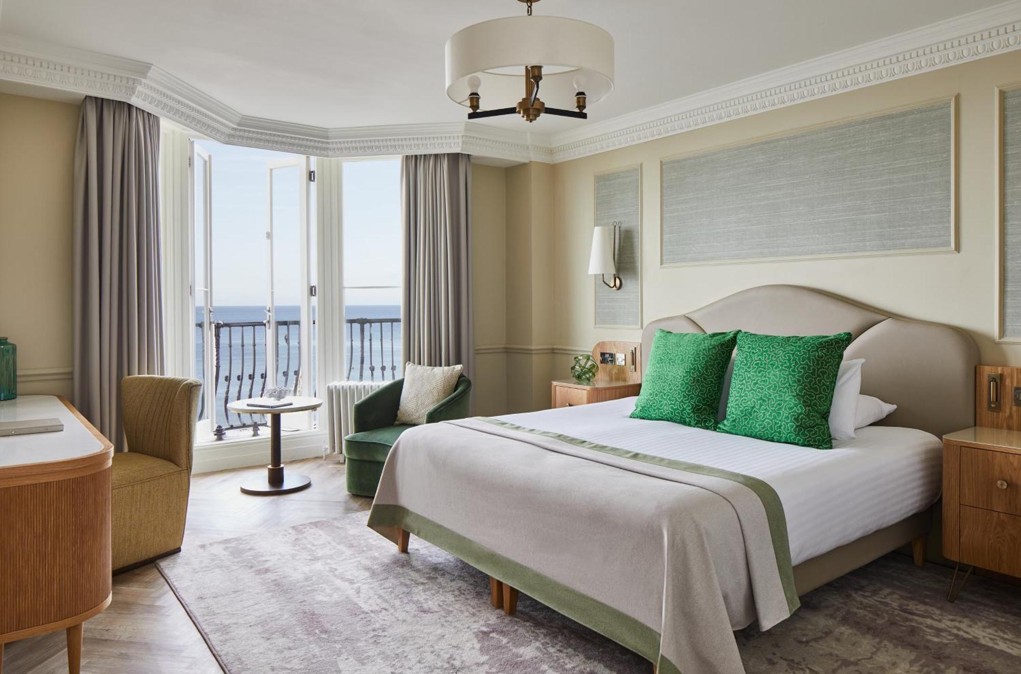The Grand Brighton Hotell Exteriör bild The photo shows a well-appointed hotel room featuring a large bed with light-colored bedding and two green decorative pillows. There is a bedside table with a lamp on either side of the bed. The room has two windows that let in natural light, and the