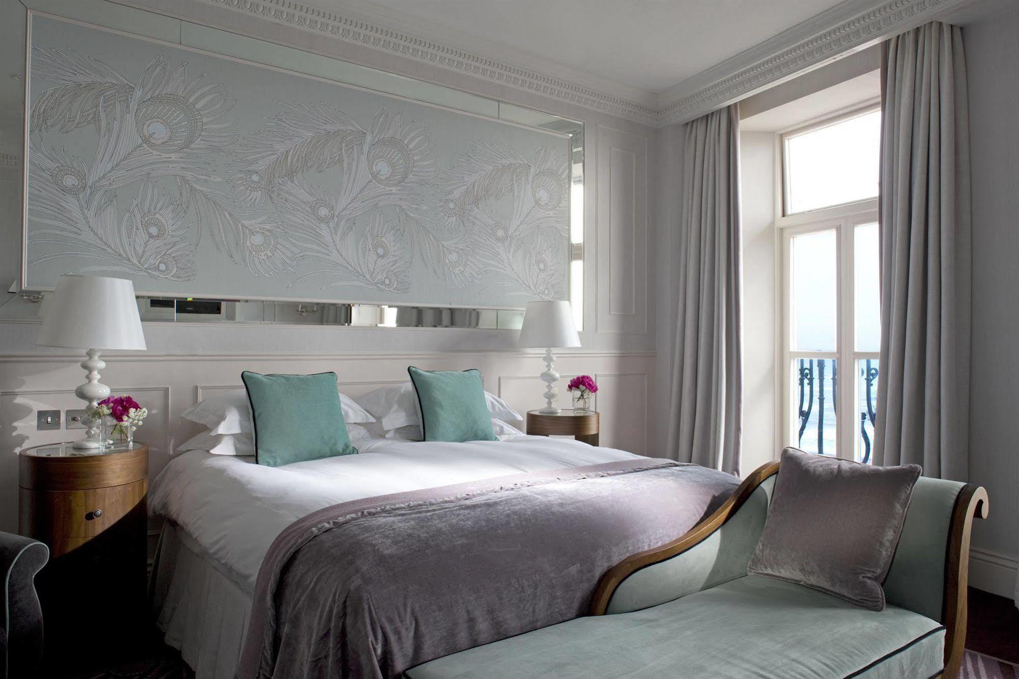 The Grand Brighton Hotell Exteriör bild The photo shows a modern and elegantly designed bedroom. It features a large bed with soft linens and two decorative pillows in a light teal color. The headboard is adorned with a subtle floral design, adding a touch of sophistication. Beside the bed