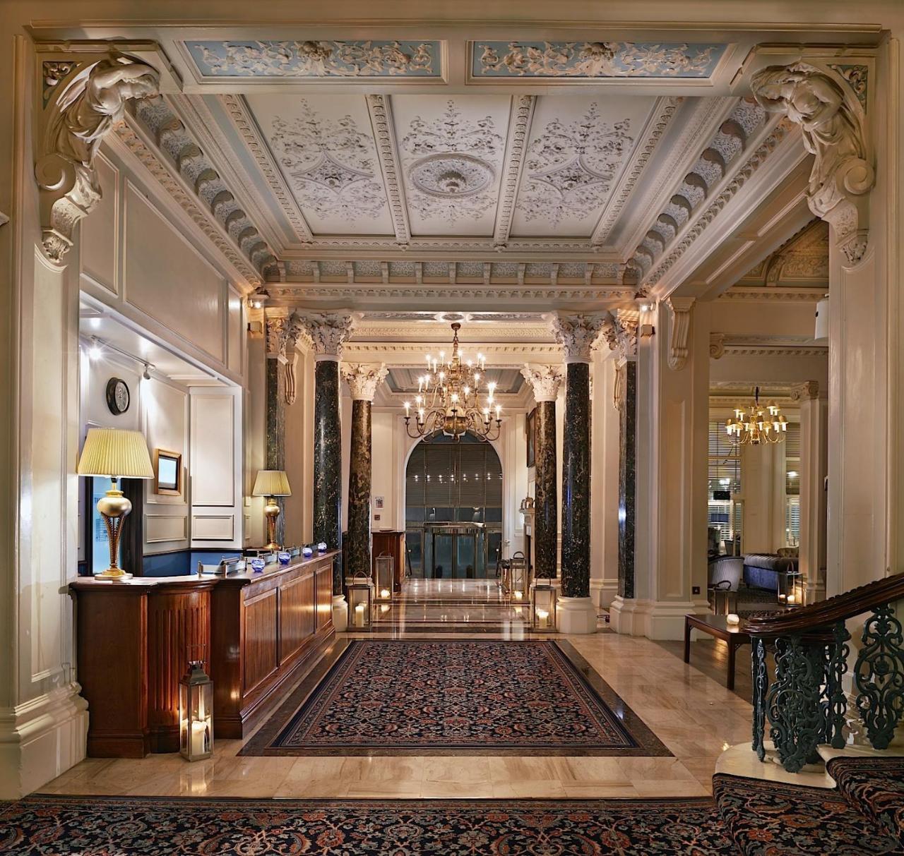 The Grand Brighton Hotell Exteriör bild The photo showcases an elegant hotel lobby. It features a reception desk made of dark wood, accented by soft lighting from lamps. The ceiling is intricately designed with decorative moldings, and a large chandelier hangs above, providing ambient ligh